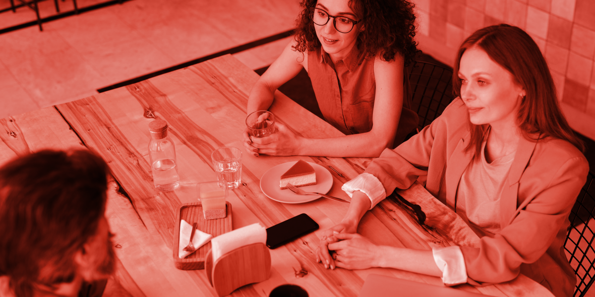 Three people sitting around a table in a meeting, viewed from above with a red brand overlay.